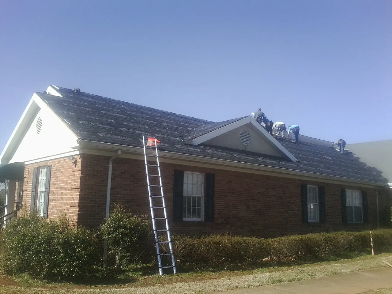 Crew tearing shingles off a brick ranch roof with a ladder set — Emergency Roof Repair work by our crew in Langley