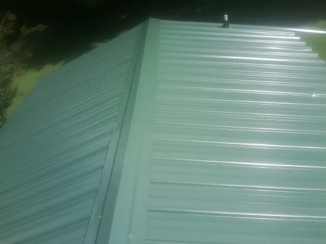 New green metal panels meeting at the ridge of a roof — Flat Roof Repair work by our crew in Langley